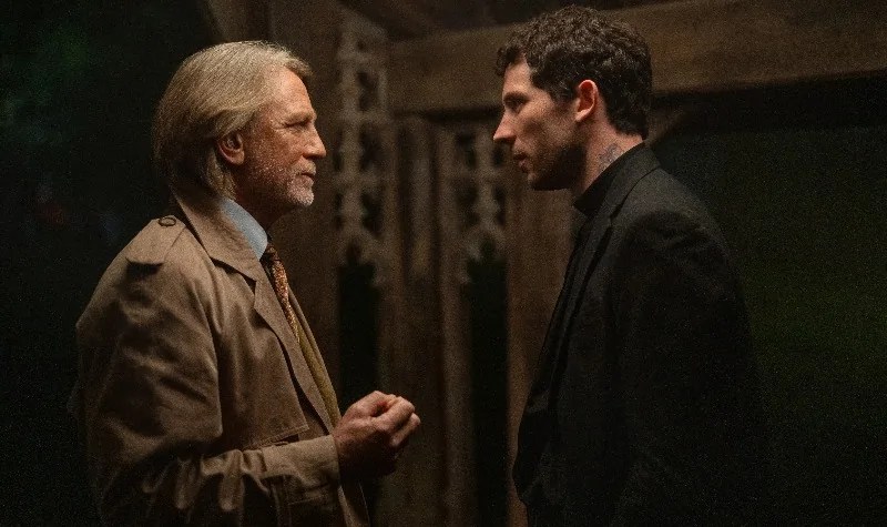 An older man in brown suit chats to an anxious priest in Wake Up Dead Man